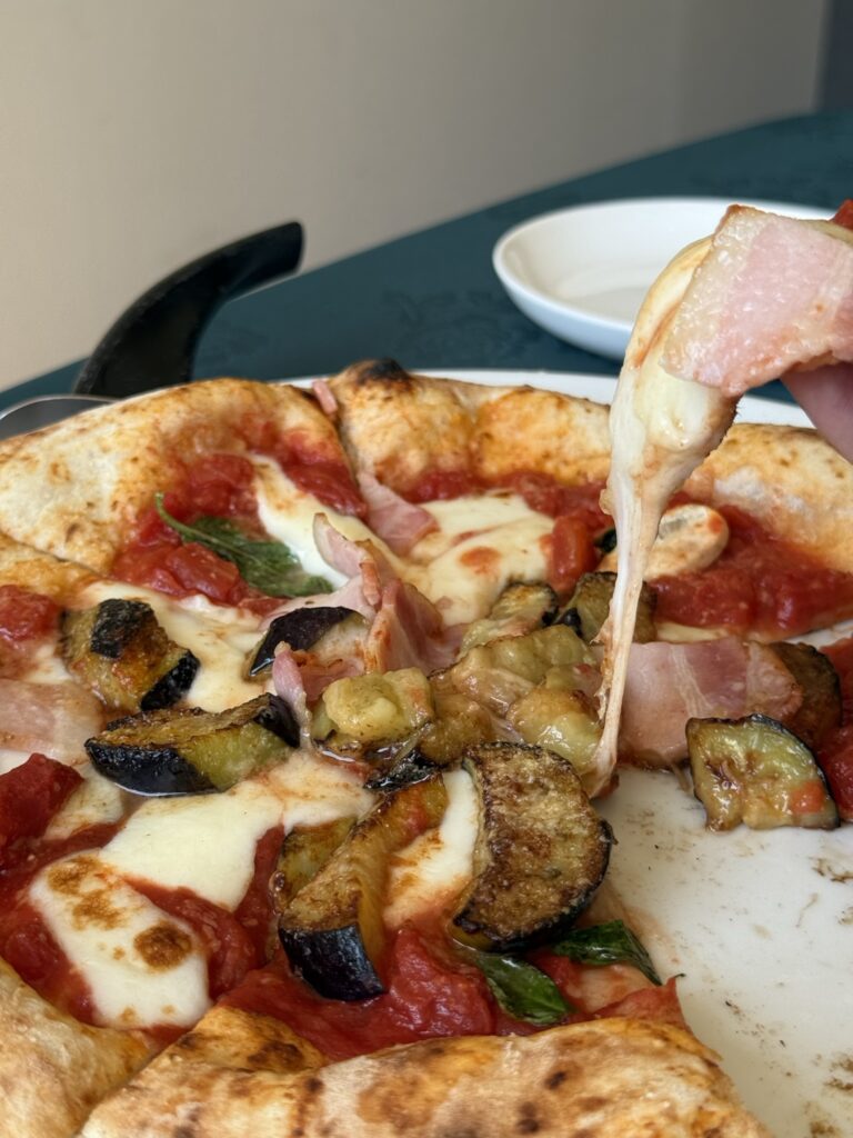 茄子とベーコンのピッツァのチーズが伸びているアップの写真